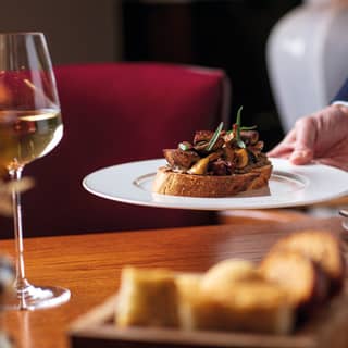 Hand placing a plate topped with mushroom bruschetta on a polished wood table