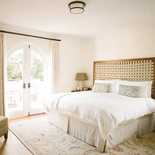 Sunlight pours through arched glazed double doors into a deluxe king bedroom at the El Encanto hotel