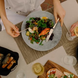 A guest enjoys Lobster Cobb salad with green beans and egg as her partner reaches for a glass of white wine, seen from above.