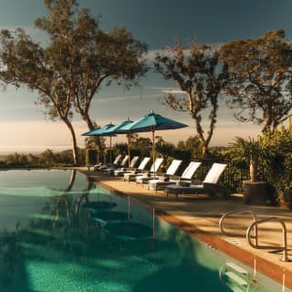 Outdoor infinity pool surrounded by sun beds and blue parasols