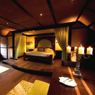 An oak-framed bed sits atop an oak dais. Bead-edged curtains divide the sleeping and sitting area with yellow velvet sofas