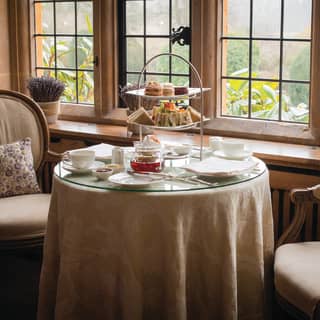 Circular table laden with afternoon tea treats, with two cream chairs either side