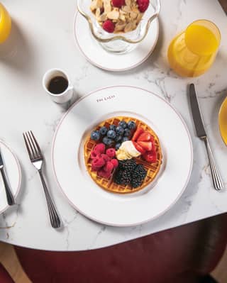 Looking down on a plate of homemade waffles with Chantilly cream and blue and red berries at a table with juice and granola.