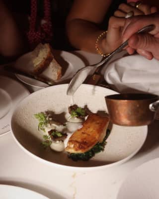 A guest spoons a white foam sauce over a plate of seared halibut and white asparagus puree, served at The LaLee restaurant.